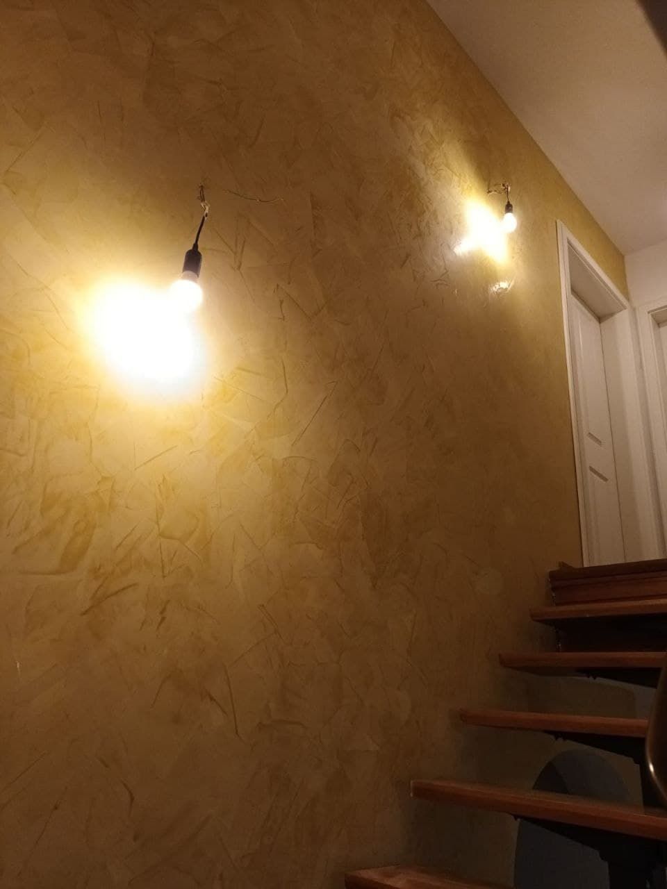 Treppenhauswand in warmem Ocker, in mehreren Lasurlagen aufgezogen, im Streiflicht zweier Wandleuchten