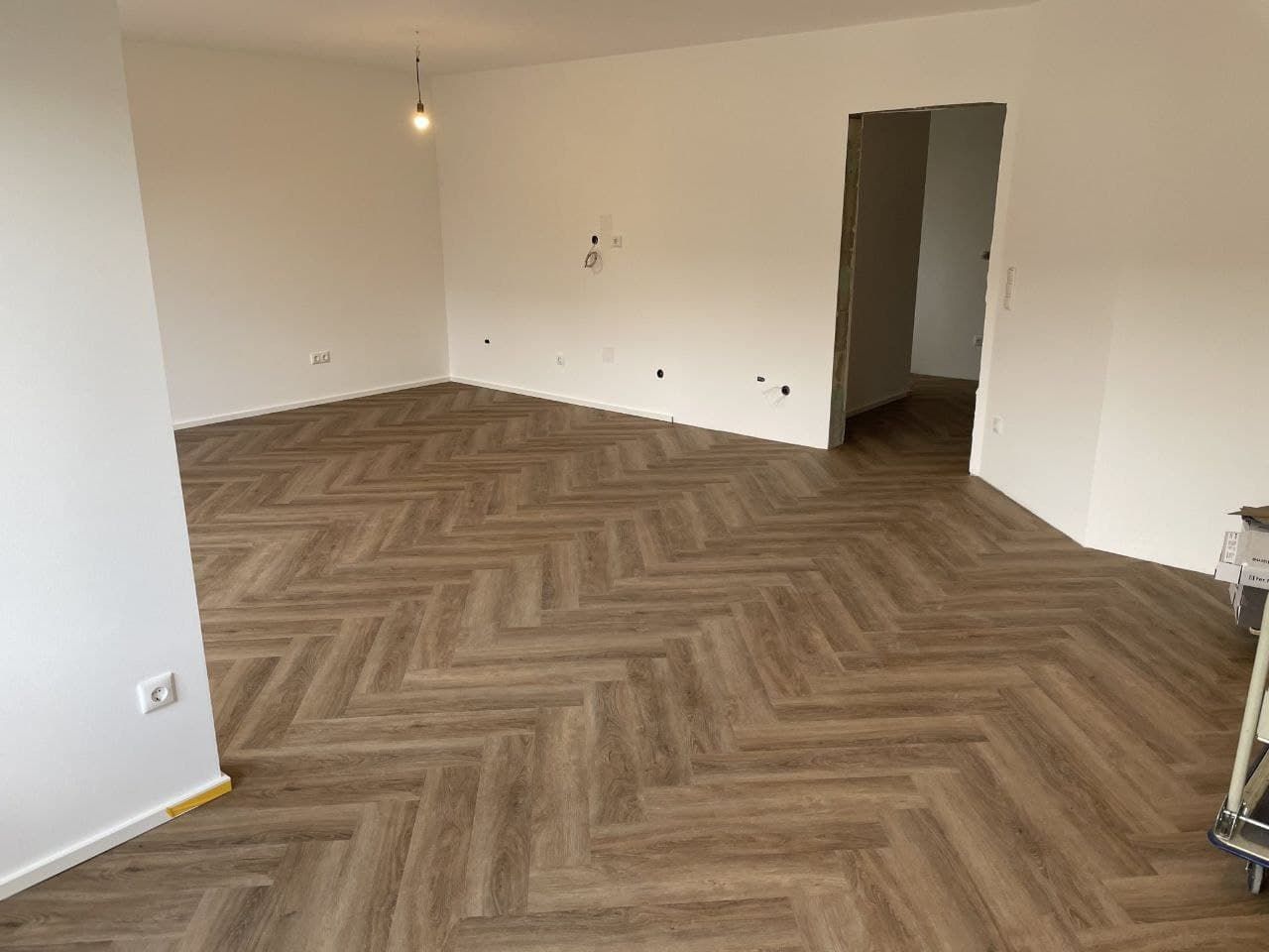 Leerer Wohnraum mit frisch gespachtelten und weiß gestrichenen Wänden und Decke sowie einem Fischgrätboden
